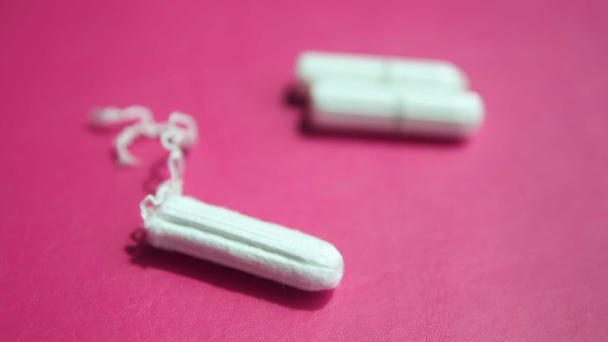 Three tampons sit on a pink surface.