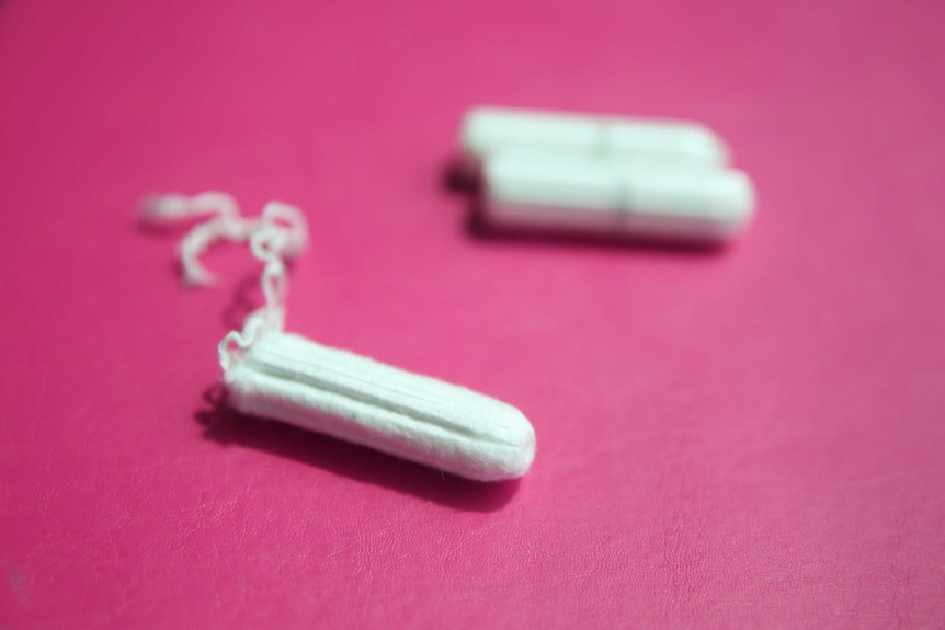 Three tampons sit on a pink surface.