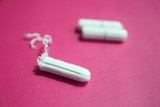 Three tampons sit on a pink surface.