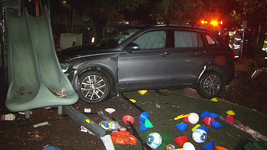 A grey station wagon with airbags deployed crashed into a green slide, with sports equipment scattered