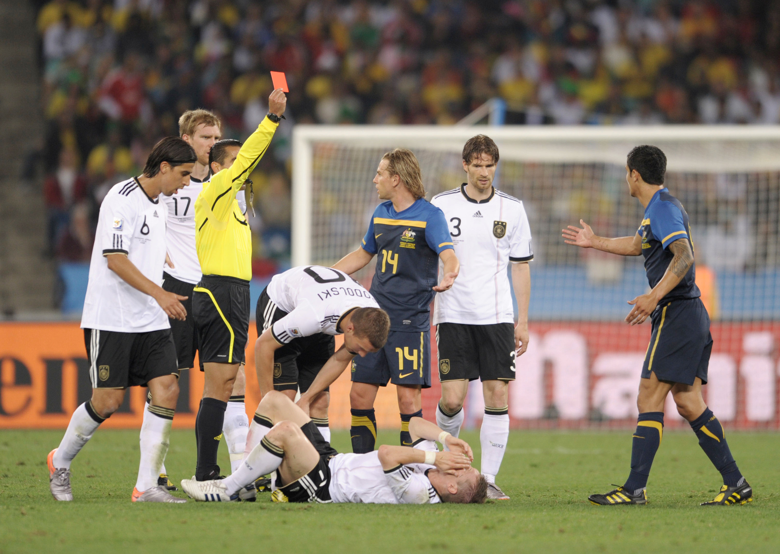 Cahill gestures in protest at a referee holding up a red card as Schweinsteiger lies crumpled on the pitch.