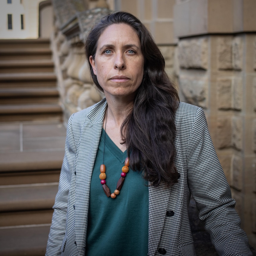 A woman sits on a sandstone banister outside a government building.