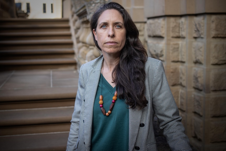 A woman sits on a sandstone banister outside a government building.