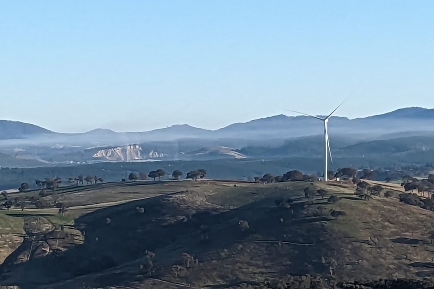 Dust hovering above the ground with a wind turbine in the foreground and hills in the background.