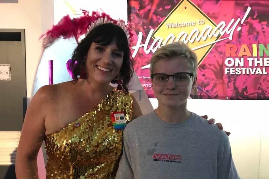 A woman with black hair and a sparkly top has her arm around a young boy in glasses.