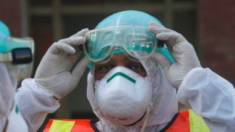 A person in a full protective suit and face mask raises their goggles.