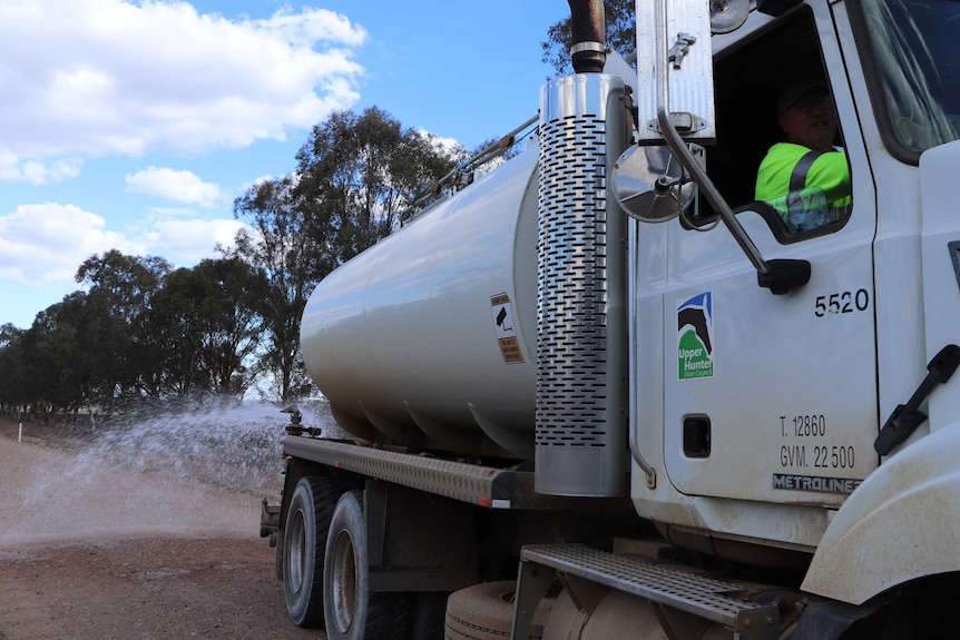 A watering truck drives along a gravel road.