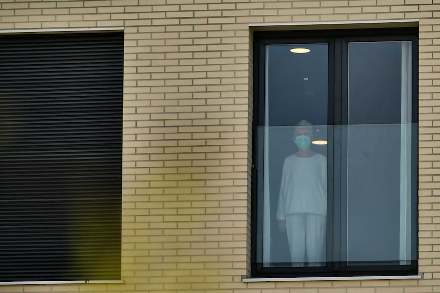 Mujer con una máscara protectora mirando por la ventana