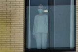 A woman wearing protection mask looks on through the window
