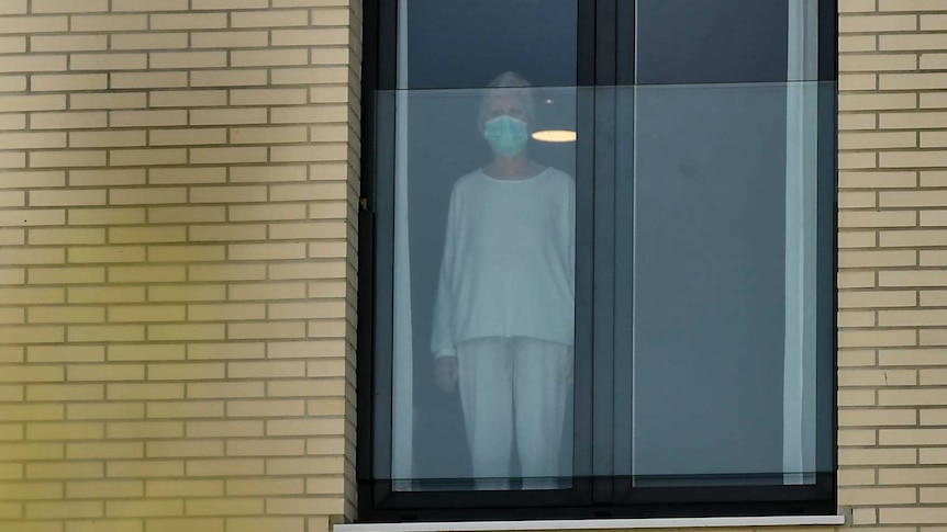 A woman wearing protection mask looks on through the window