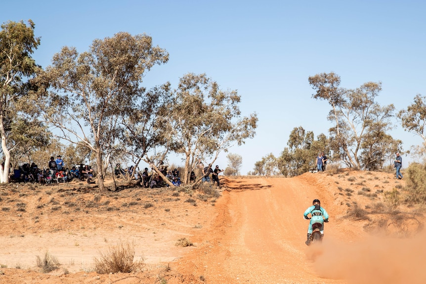 A motorcycle on a dirst track with spectators either side.