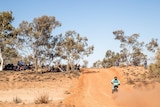 A motorcycle and rider on a red dirt track in the Finke Desert Race.