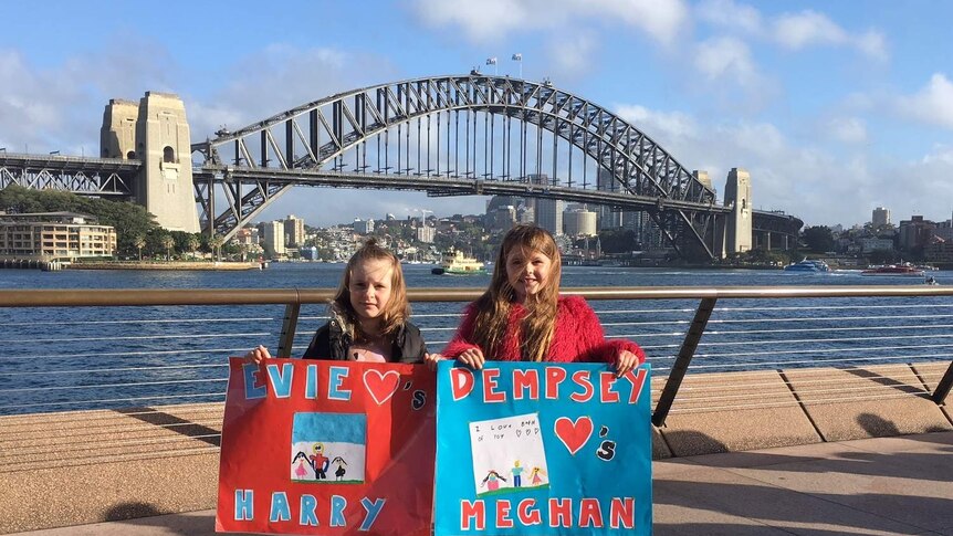 two young girls standing on harbour holding signs