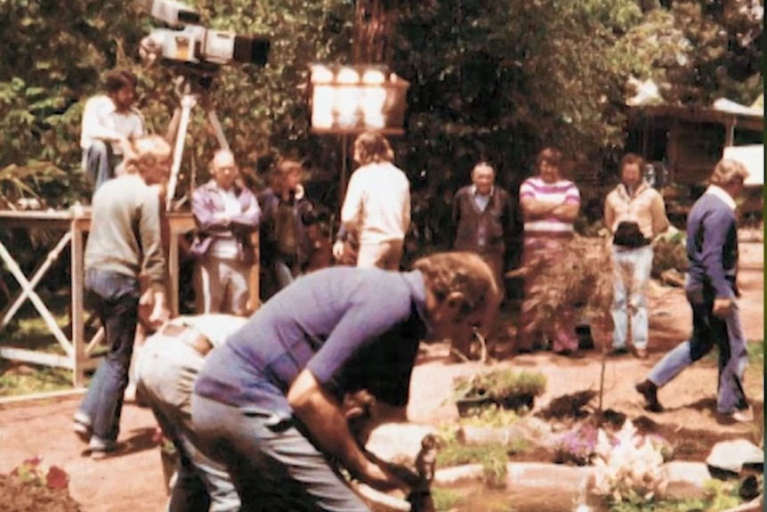 Grainy photo of eleven men at work in garden with old TV camera and lights set up.