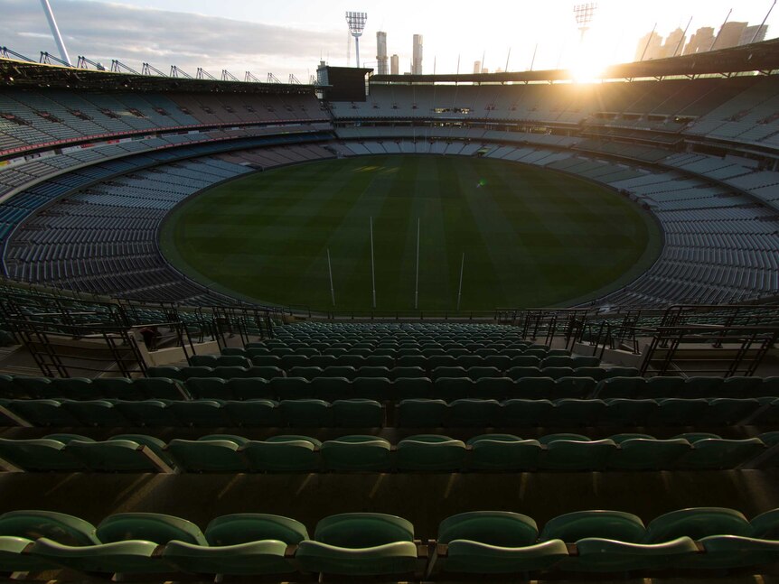 The sun goes down behind the Melbourne Cricket Ground light towers and city buildings