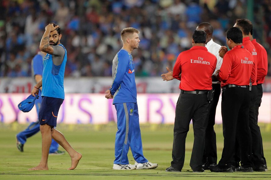 Umpires talk to Australia's David Warner (2L) at the third T20I, as India's Virat Kohli walks off.