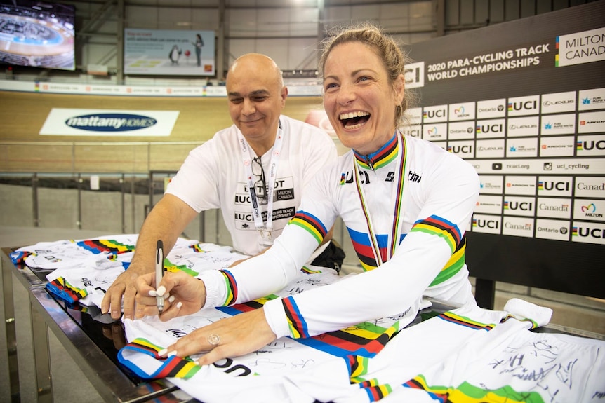 Emily Petricola sits at a table and smiles while signing jerseys.