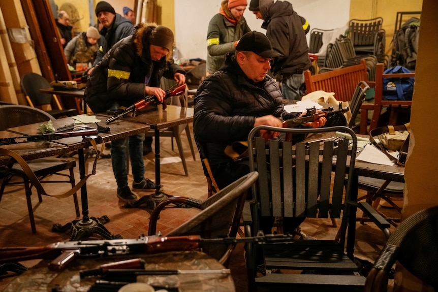 People in a small room with yellow armbands inspect and practice with rifles.