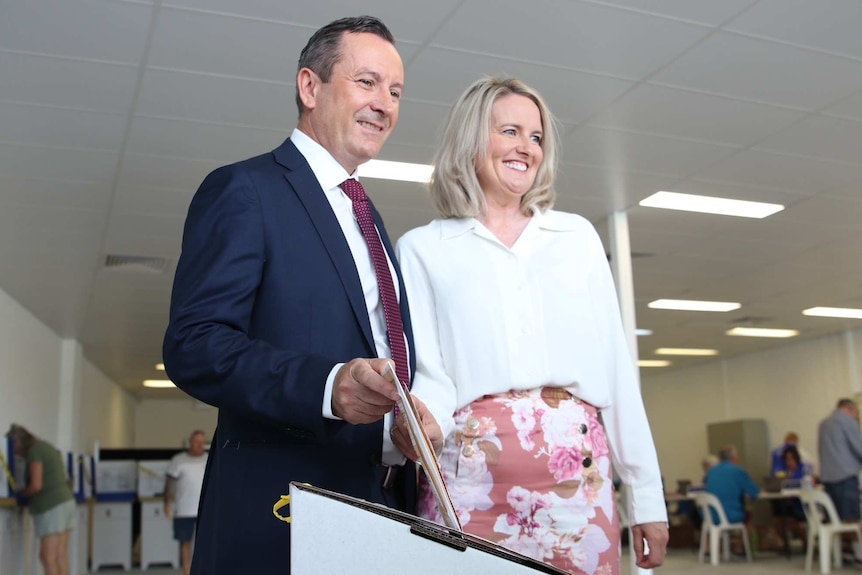 Mark McGowan and his wife Sarah McGowan stand side by side holding their votes above a ballot box.