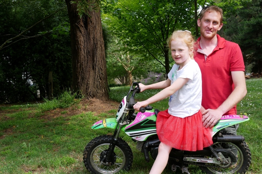 A man and young girl with a child's motorbike.