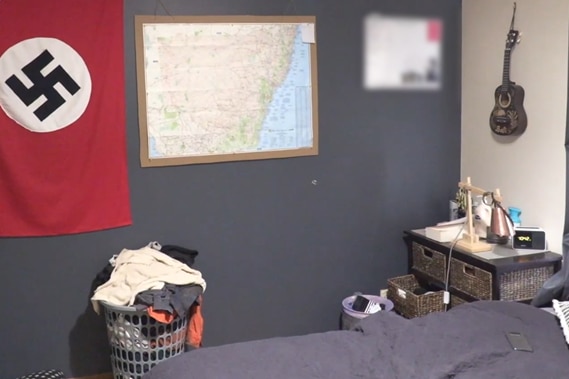 A nazi flag, map of New South Wales, calendar and ukulele hang on the walls of a small bedroom.