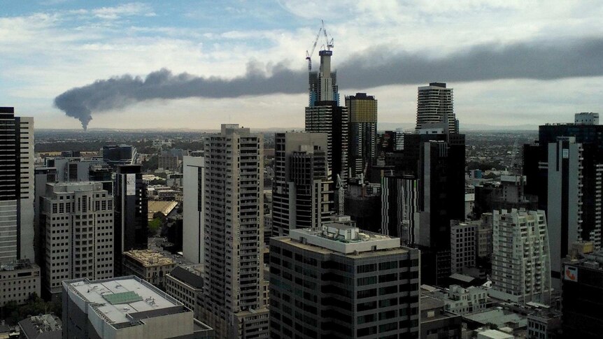 Photo of a distant plume of smoke spreading across Melbourne, taken from Melbourne city office block through city buildings.