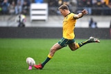 A Wallabies player attempts to kick the ball on a kicking tee with his right foot against New Zealand.