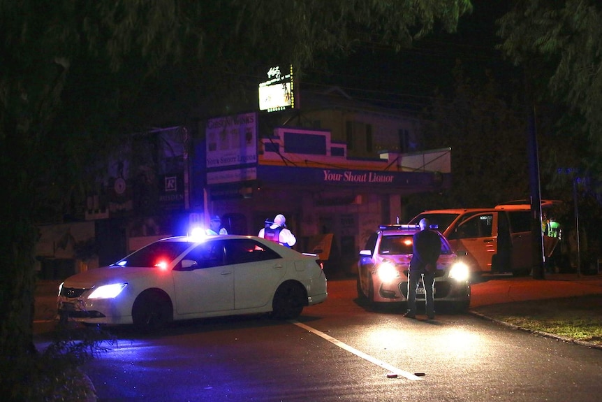 A wide shot showing police cars blocking a street at night in Mount Lawley with a liquor store in the background.