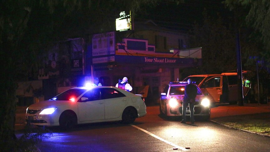 A wide shot showing police cars blocking a street at night in Mount Lawley with a liquor store in the background.