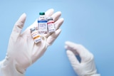 A white gloved hand hold three small labelled vials filled with clear liquid