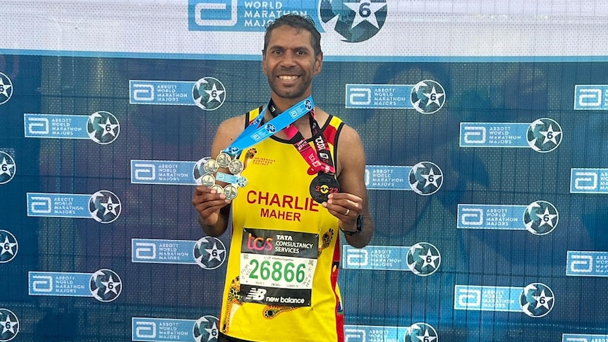 A man smiles holding his marathon medals