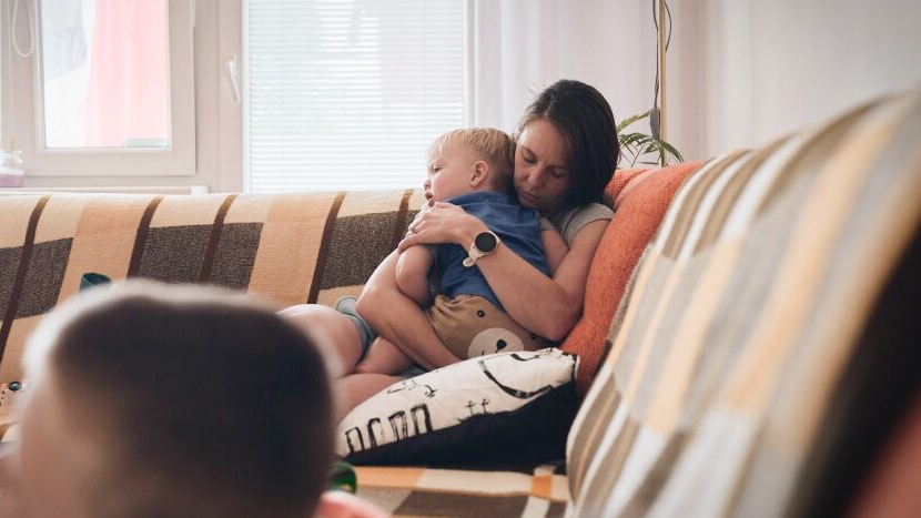 A young boy is watching TV on the lounge while her mother and baby cuddle together. 