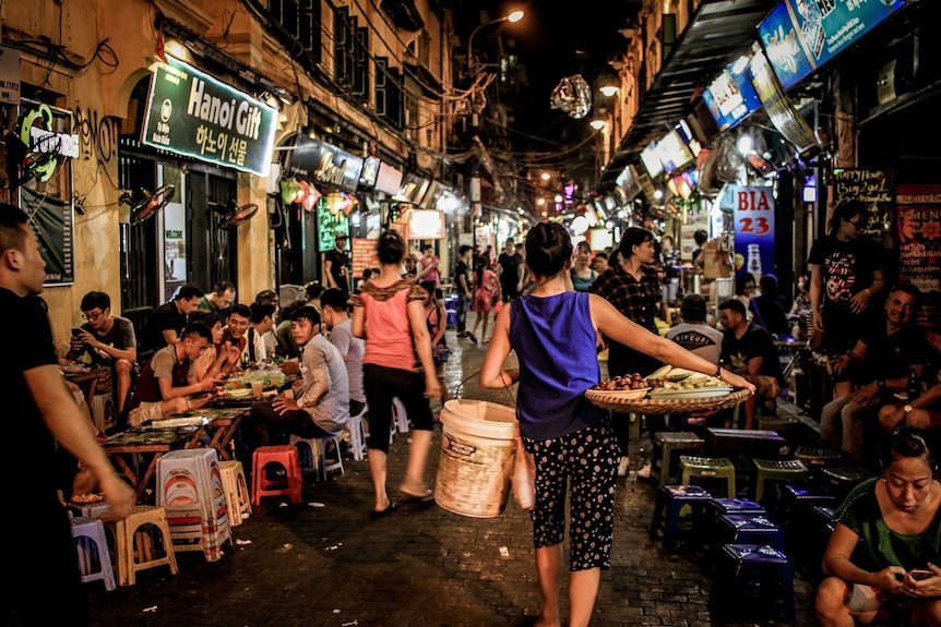 A busy street in Hanoi filled with people on plastic seats eating food