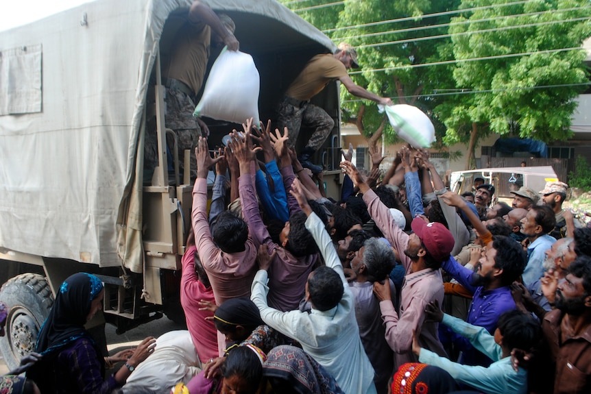 Two soldiers distribute bags of aid from the back of a truck as tens of people reach out to receive aid.