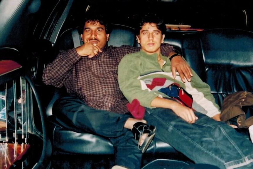 Vick Singh sits, right, in a car next to his uncle, left, who has his arm around him. It appears to be a film photo.