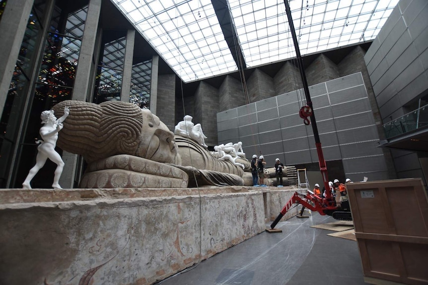 Workers clamber over a giant reclining Buddha in the NGV foyer.