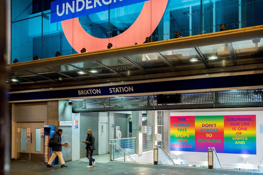 The entrance of Brixton Station in London with a series of three rainbow artworks hung above the escalators