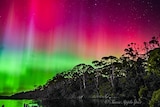Pink and green lights of an Aurora Australis over water 