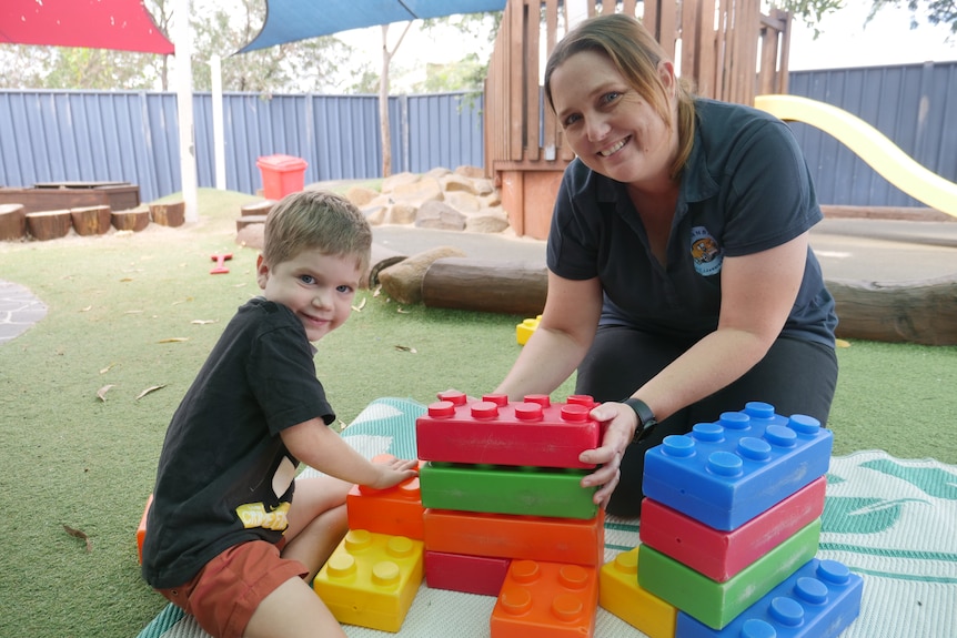 A woman and a young boy sit on a mat stacking building blocks
