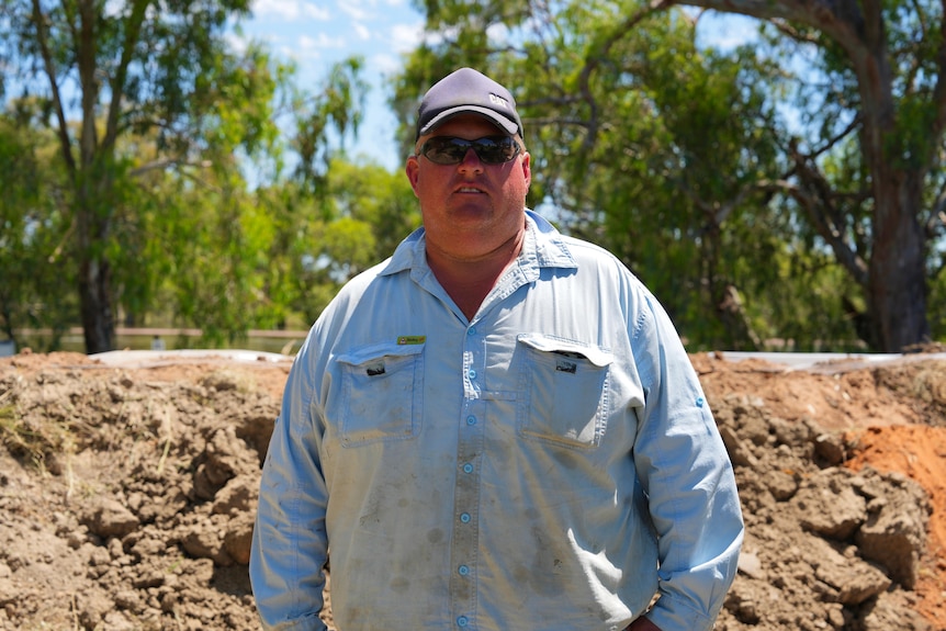 A white man wearing a blue shirt and dark hat with sunglasses at Menidee standing in front of a levee.