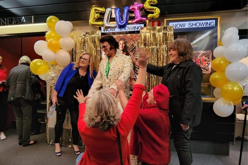 An Elvis Presley impersonator surrounded by people and balloons. 