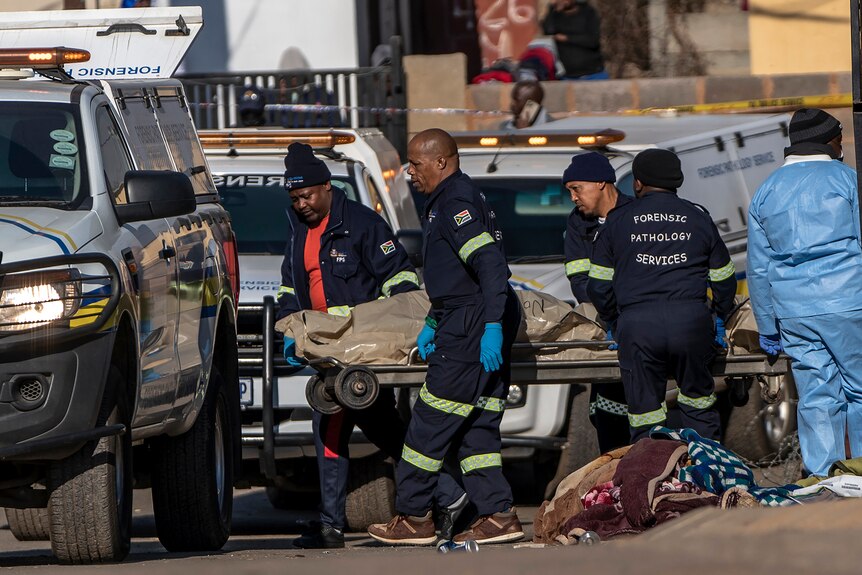 A team of four forensic police officers carry a body bag to a police van after a mass shooting