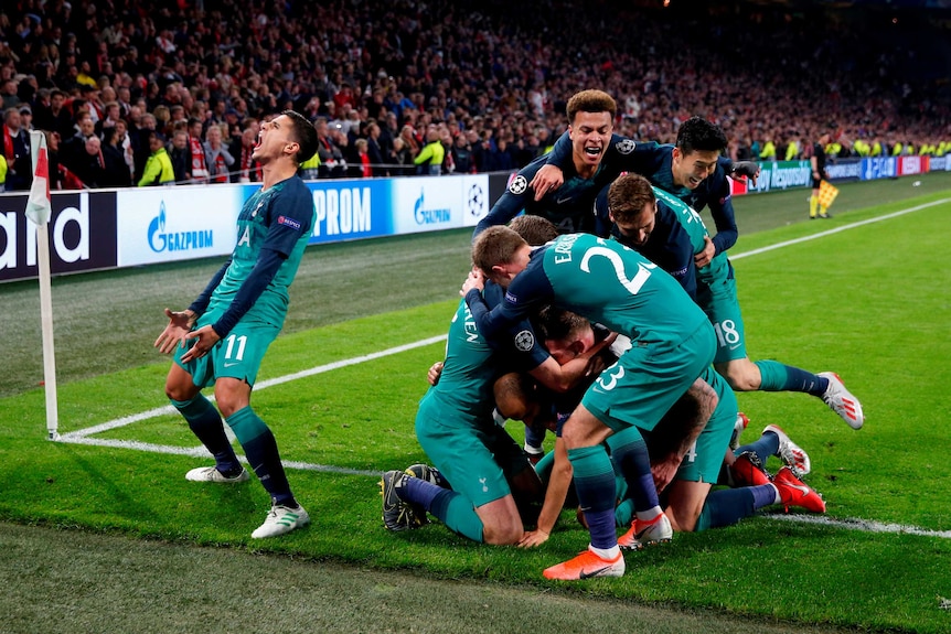 Football players pile on to each other in celebration after a last-minute goal while another player pumps his fists