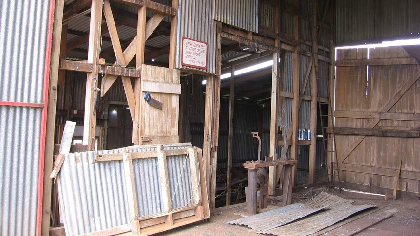 A view inside an old tin shed, showing missing pieces of iron walls and doors as well as bird poo