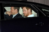 Prince Harry in a black car with another man beside him.