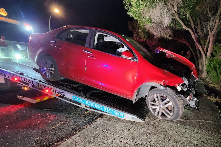 A damaged red car on the back of a two truck.