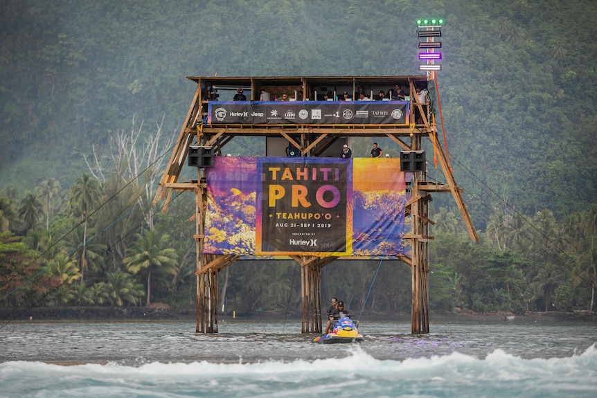 A wooden judging tower in the water with Tahiti Pro signage.