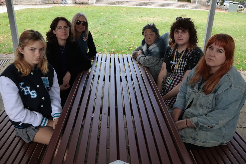Seis jóvenes sentados en una mesa encubierta en un parque, mirando a la cámara