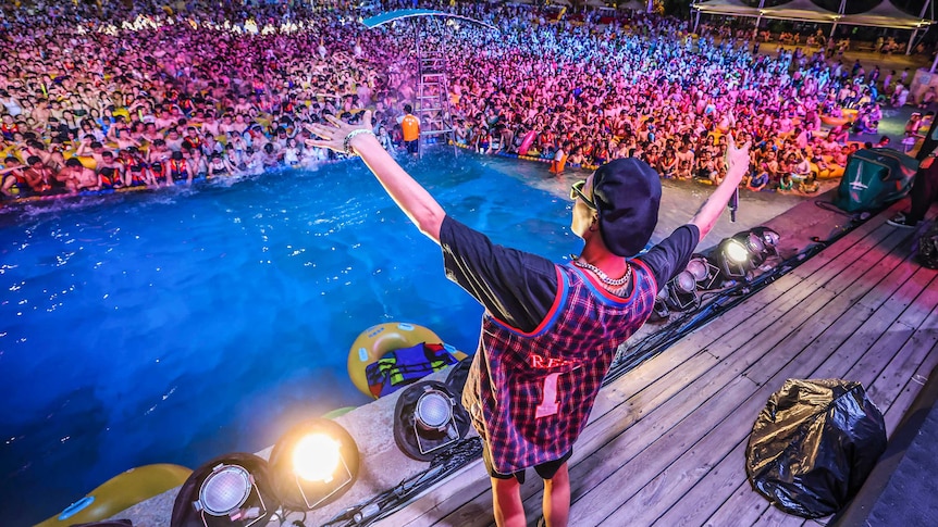 A person on stage gestures to a huge crowd of people in a pool in Wuhan, during a music festival.