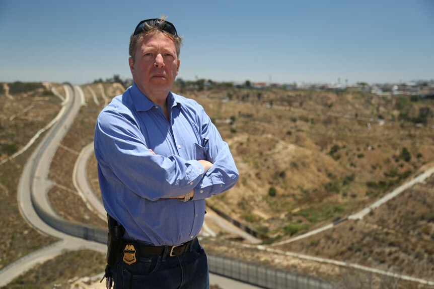 National Border Patrol Council San Diego representative Chris Harris stands in front of the fence between the US and Mexico.